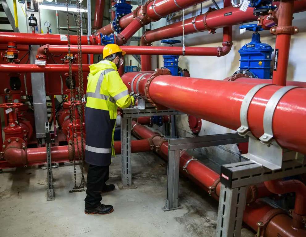 A man in yellow jacket standing next to pipes.